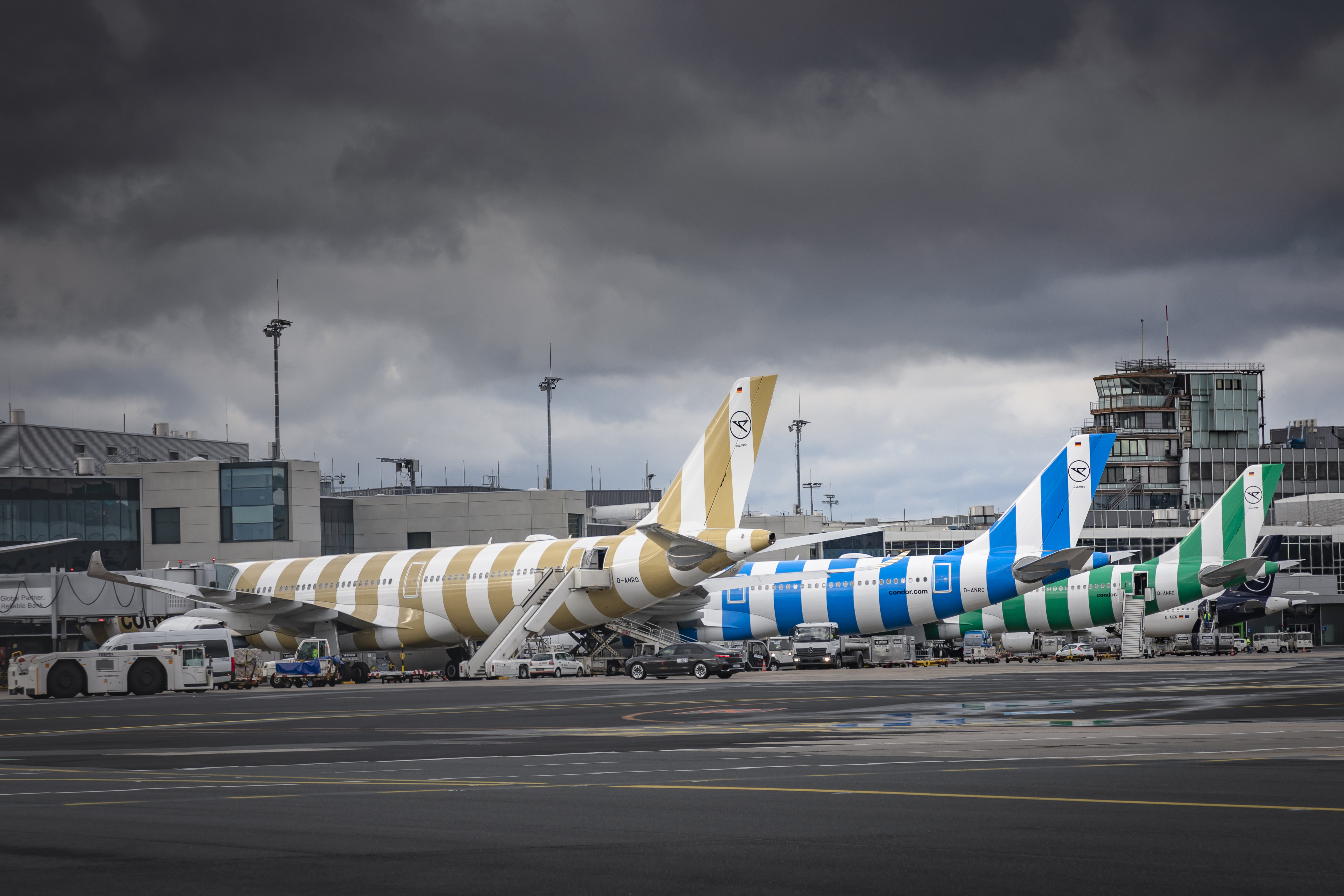 Condor aircraft with striped liveries on the airport apron beneath a cloudy sky.