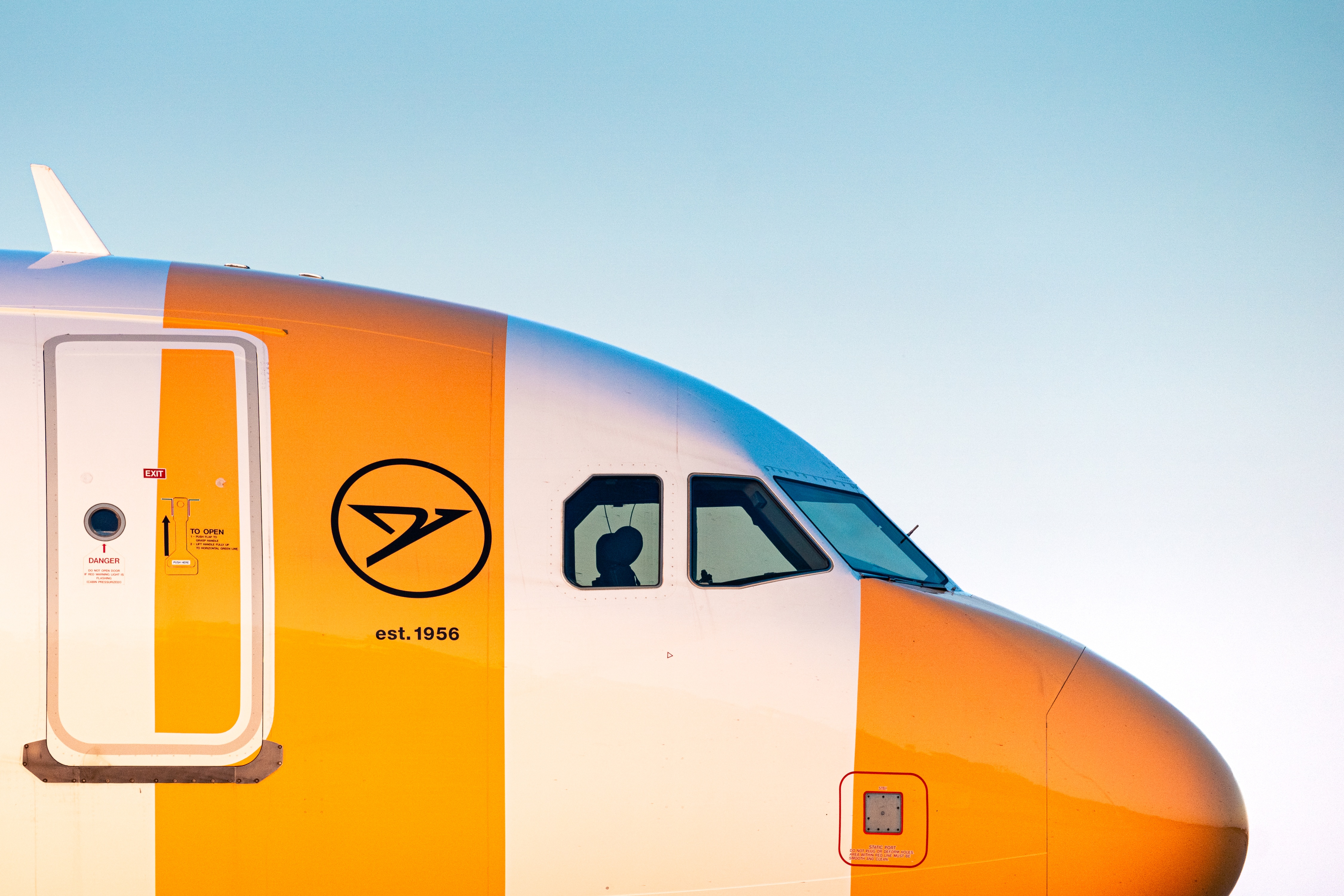 A close-up of the nose of a passenger aircraft in yellow-and-white-striped livery, showing the cockpit windows and aircraft door.