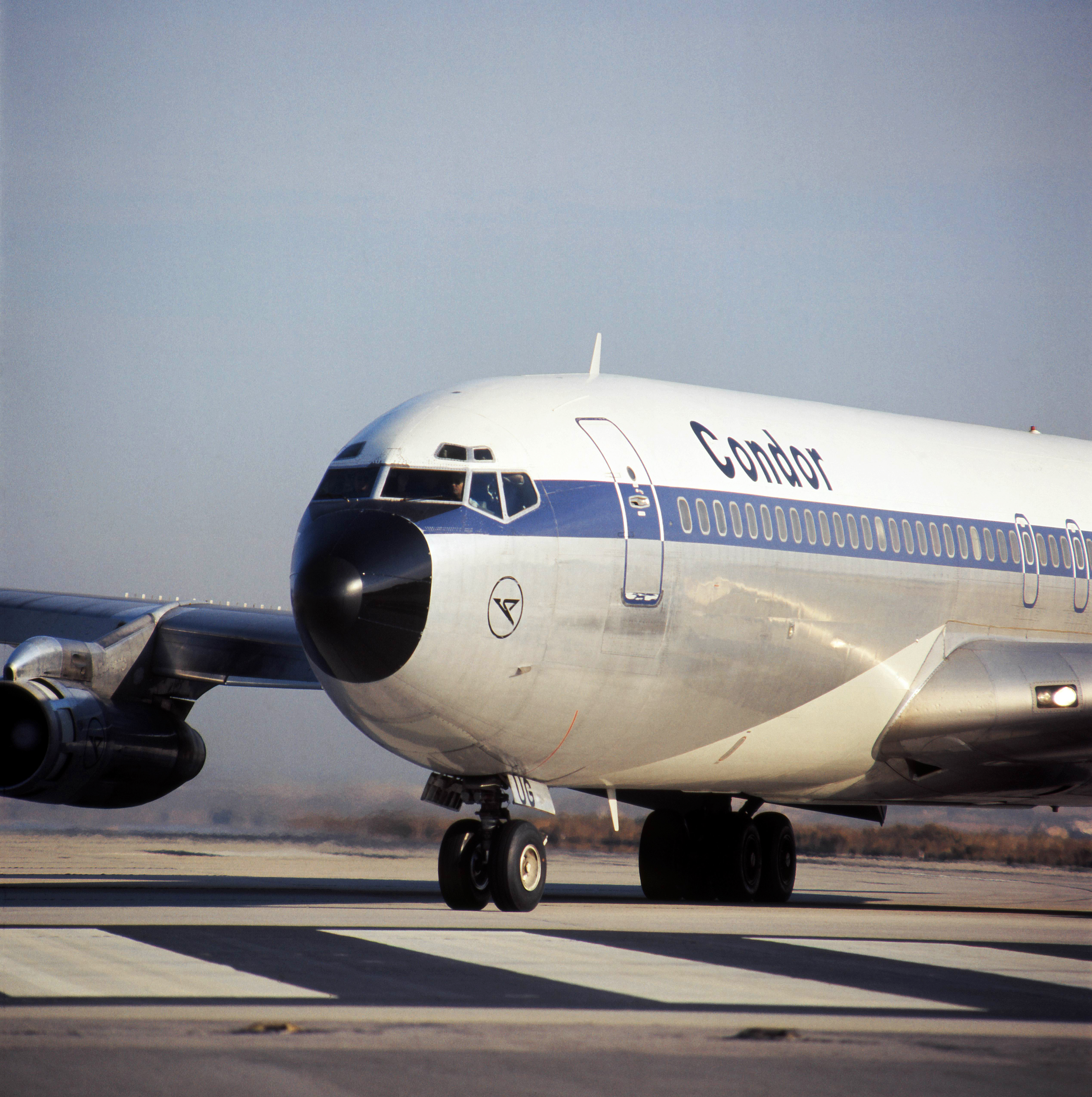 The picture shows the nose of a vintage passenger aeroplane with a blue and white livery on an airport apron. Visible are the cockpit windows, part of the aircraft fuselage and the engines. The aeroplane is shown at an angle from the front.