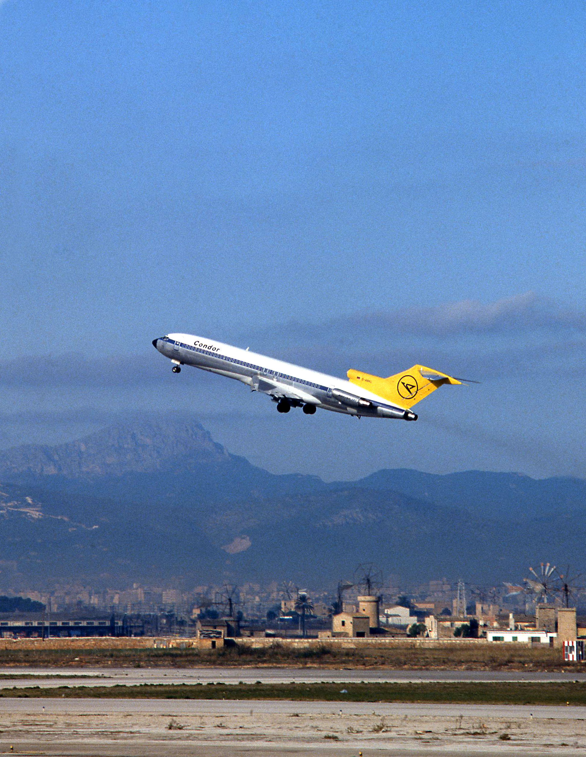 Historic passenger aircraft with a yellow tail flying over a mountainous landscape.