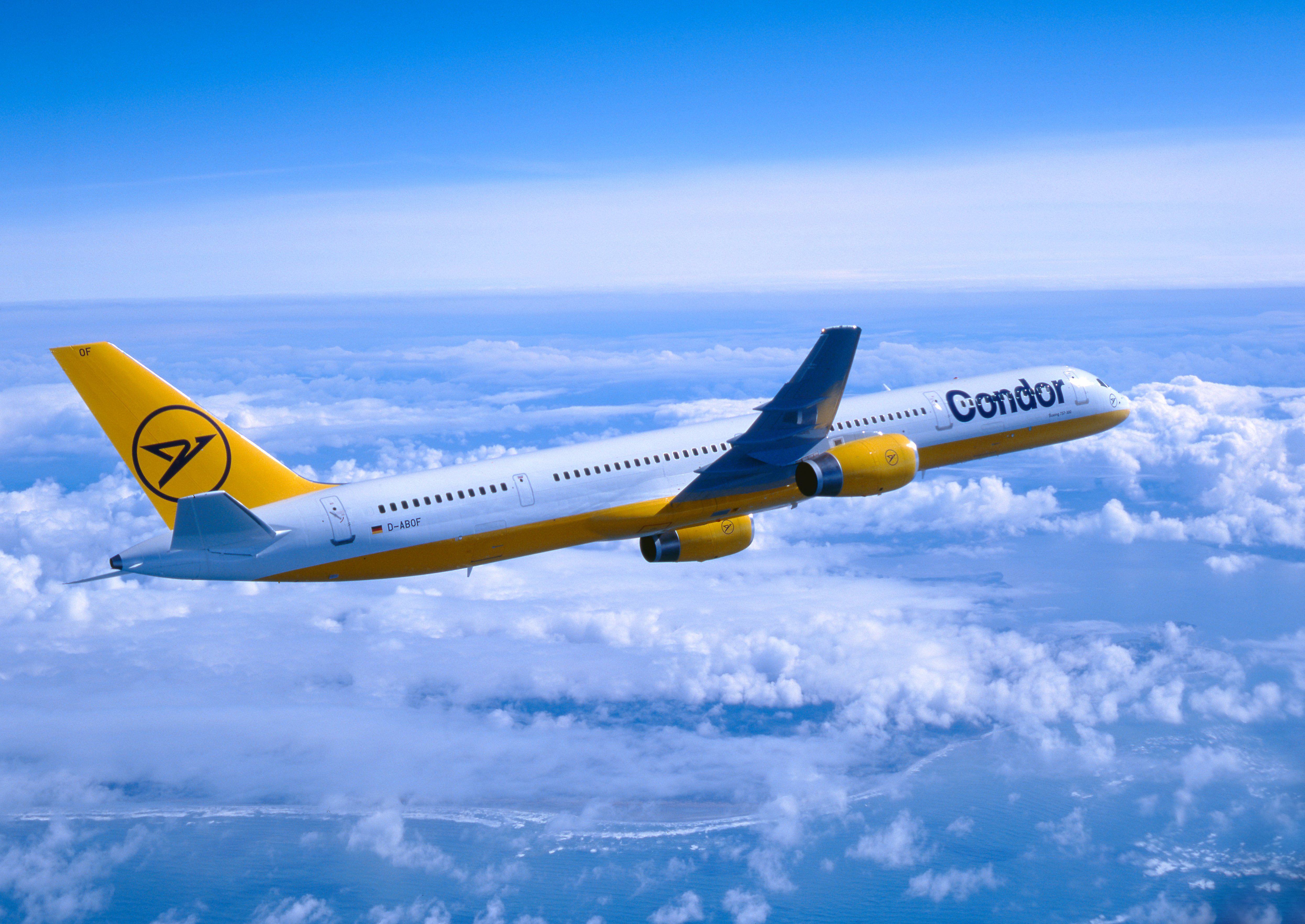 Image d'époque représentant un avion Condor aux couleurs jaune et blanc survolant une épaisse couche nuageuse. L'avion est pris de côté sur fond de ciel bleu.